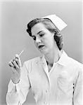 1950s WOMAN NURSE CHECKING TEMPERATURE ON THERMOMETER