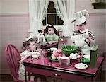 1940s 1950s BOY TWO GIRLS AT KITCHEN TABLE BOY IN TOQUE COOKING ONE GIRL EATING TODDLER AND PUPPY IN HIGH CHAIR