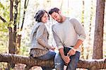 Couple sitting on fallen tree opening bottle of rose wine in forest