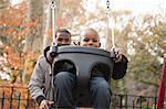 Father pushing toddler son on park swing