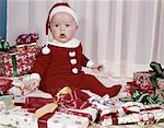 1960s AMAZED BABY IN SANTA SUIT SITTING AMONG WRAPPED PRESENTS