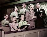 1950s TWO FAMILIES PARENTS CHILDREN IN CHURCH PEWS SINGING FROM HYMNAL BOOKS