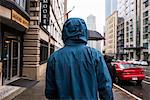 Rear view of young man strolling on rainy street, Seattle, Washington State, USA