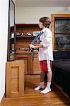 Boy practicing tying large tie in bedroom mirror