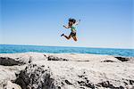 Young woman jumping over rocks, Scarborough Bluffs, Toronto, Ontario, Canada