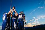 Teenage and young male american football team celebrating and holding up ball
