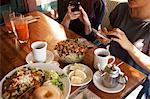 Cropped shot of  female friends texting on smartphones in vegetarian restaurant