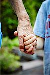 Cropped close up of senior woman and grandson hands holding in park