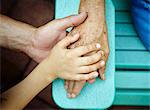 Cropped close up of senior woman, son and grandson hands touching in park