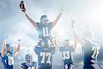 Teenage and young male American football team celebrating on pitch