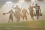 Rear view of teenage and young male american football team celebrating in stadium