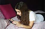 A teenage girl listening to music on her touch pad on her bed