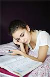 A teenage girl doing homework on her bed