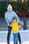 young mother and her son ice skating together at outdoor skating rink at winter