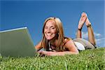 Woman with computer in the grass towards blue sky