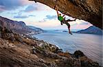 Male climber climbing overhanging rock against beautiful view of coast below