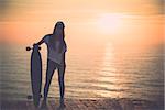 Beautiful fashion skater girl posing with  a skateboard at the sunset