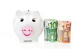 Happy piggy bank with hundred and fifty eur notes bundle next to it isolated on white background. Saving concept.