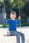 smiling positive little boy swinging in the park at summer
