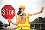 Female construction apprentice holding a stop sign and directing traffic.