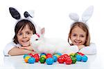 Happy kids at easter time - wearing bunny ears and guarding their white rabbit and colorful eggs