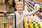 smiling positive boy at the supermarket with shopping cart and choosing juice