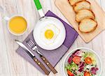 Healthy breakfast with fried egg, toasts and salad on white wooden table