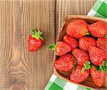 Fresh ripe strawberry in bowl over wooden table background. Top view