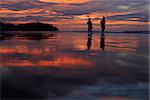 Silhouettes of two children on the beach during sunset