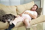 Unshaven middle-aged man asleep on the couch with his dog.