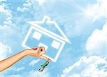Hand holding house icon and key. Background of blue sky, clouds and sun