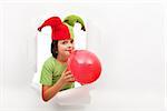 Happy boy with funny hat celebrating with a balloon - peaking through a torn hole in paper