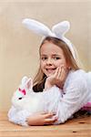 Happy girl in bunny costume holding her white rabbit - laying on wooden floor