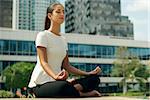 Young stressed hispanic business woman doing yoga outside office building, sitting in lotus position with hands on knees in the street. Concept of long working hours and need of stress free break