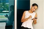 Young business woman using smartphone and taking notes on display with digital pen. The girl is outside office, leaning on a wall of building with reflections on window