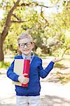 smiling little schoolboy in glasses holding book ready to go to school, back to school concept