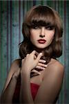 Stylish, luxury, brunette girl with beautiful, smooth hairstyle with straight fringe wearing red lipstick and astin top. She has got her hands on the chest.