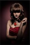 Brunette, stunning, gorgous woman in red dress. She has got smooth hairstyle with straight fringe covering her eyes. She is wearing big old fashioned necklace.