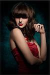 Pretty, mysterious, gorgeous woman with smooth brown hair with straight fringe wearing red, satin top, big old necklace and red lipstick, her eyes are in shadow.