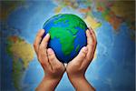 Ecology concept with earth globe in child hands against blurry world map