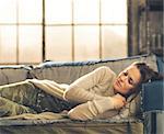 Cat-nap on a sofa. An elegant brunette woman napping on a sofa in a loft, curling her hands under her chin. Urban chic ambiance.