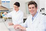 Scientist working attentively with laptop and another with beaker in laboratory