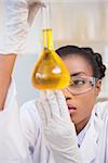 Scientist examining petri dish with orange fluid inside in laboratory