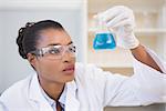 Scientist examining petri dish with blue fluid inside in laboratory
