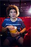 Young man watching a film and eating pop corn at the cinema