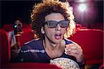 Young man watching a 3d film and eating popcorn at the cinema