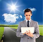 Businessman holding a tablet computer against road leading out to the horizon