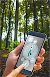 hand holding smartphone against young plant against tree trunks in forest
