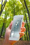 hand holding smartphone against lush trees in the forest