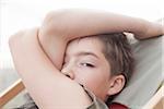 Close-up portrait of boy sitting in a deckchair looking at camera, with arm covering face, Vendome, Loir-et-Cher, France